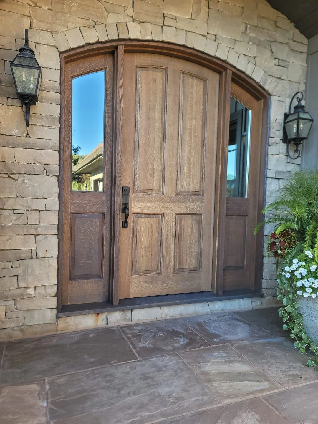 Arched wood exterior door with glass sidelights in a stone entrance